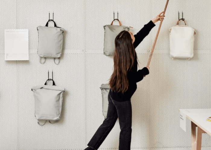 A Woman Reaching for a QWSTION Backpack that is Hanging on the Wall