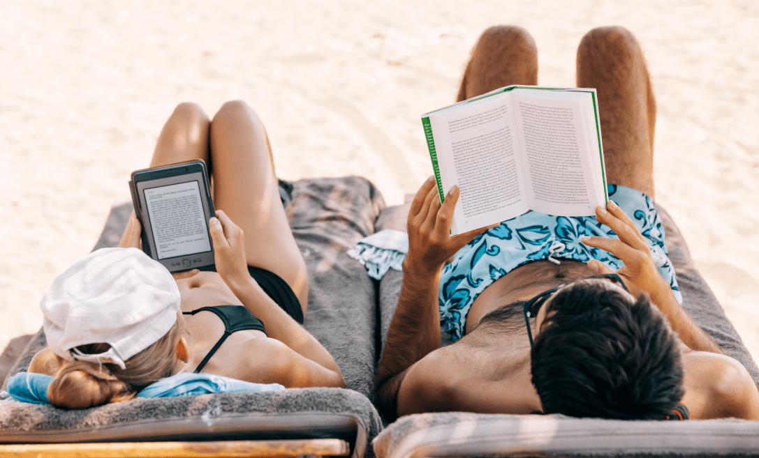 a women reads an ebook and a guy reads a printed book on a beach
