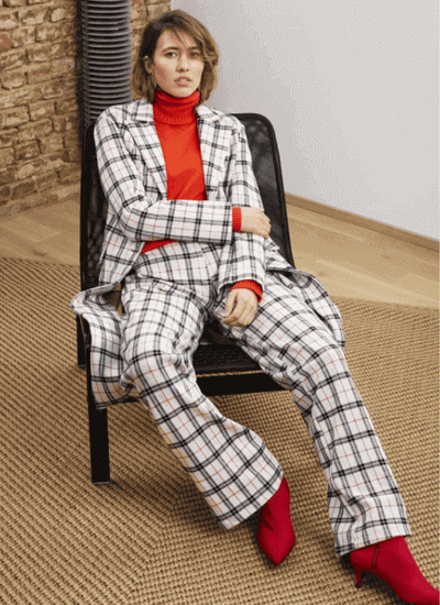 Eine Frau im karierten Hosenanzug, mit roten Schuhen und Pulli von Kleiderei
