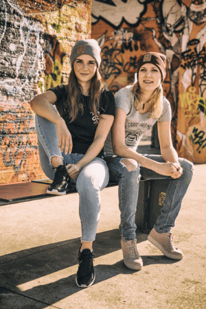 Zwei junge Frauen in Jeans, T-shirt und Mütze von Roka Fair Clothing